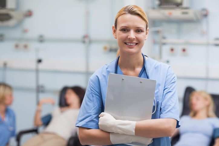 A smiling female phlebotomist holding a clipboard greeting patients after medical office specialist training. Learn more about the 3 phlebotomy best practices.