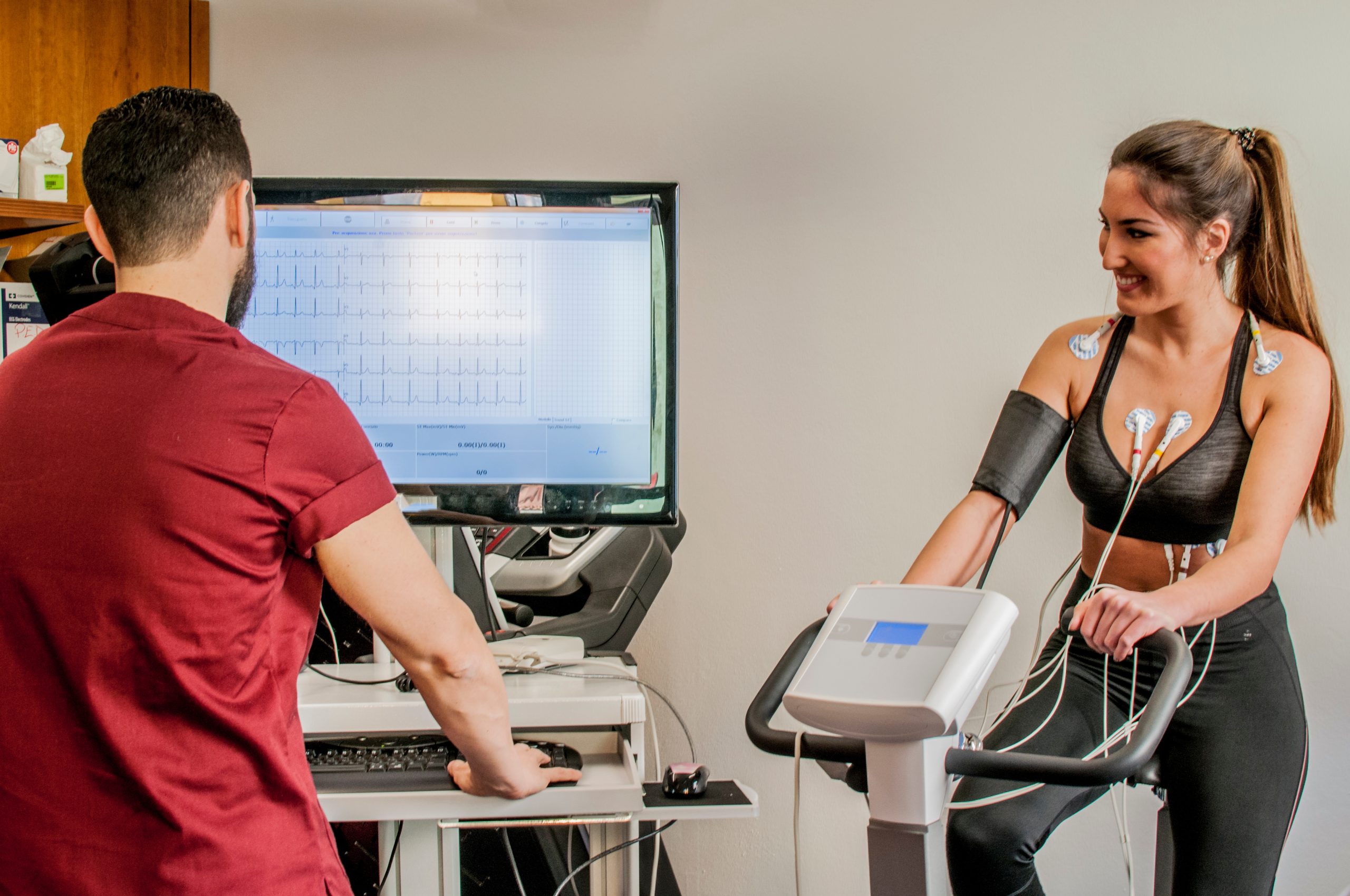 women on exercise machine and man monitoring her heart.