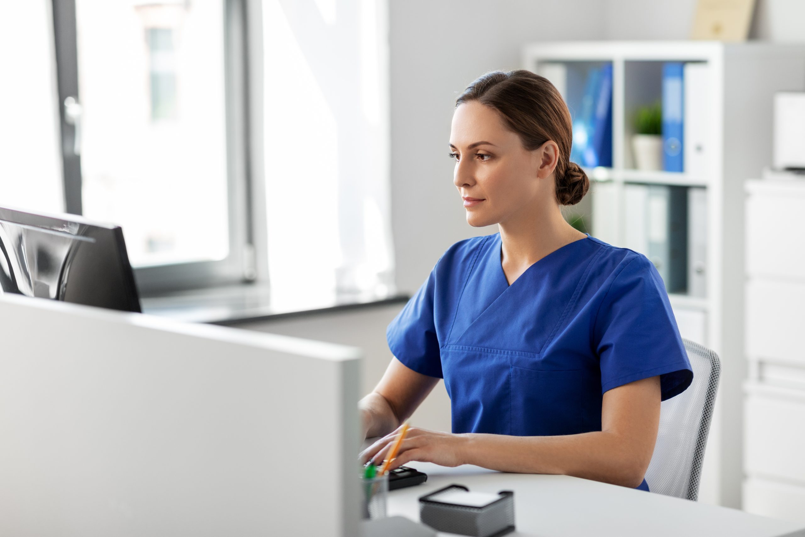 woman sitting at a desk in scrubs on a computer